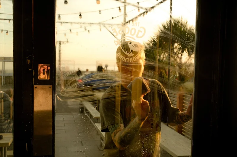 Man reflected in glass door looking out at beach.